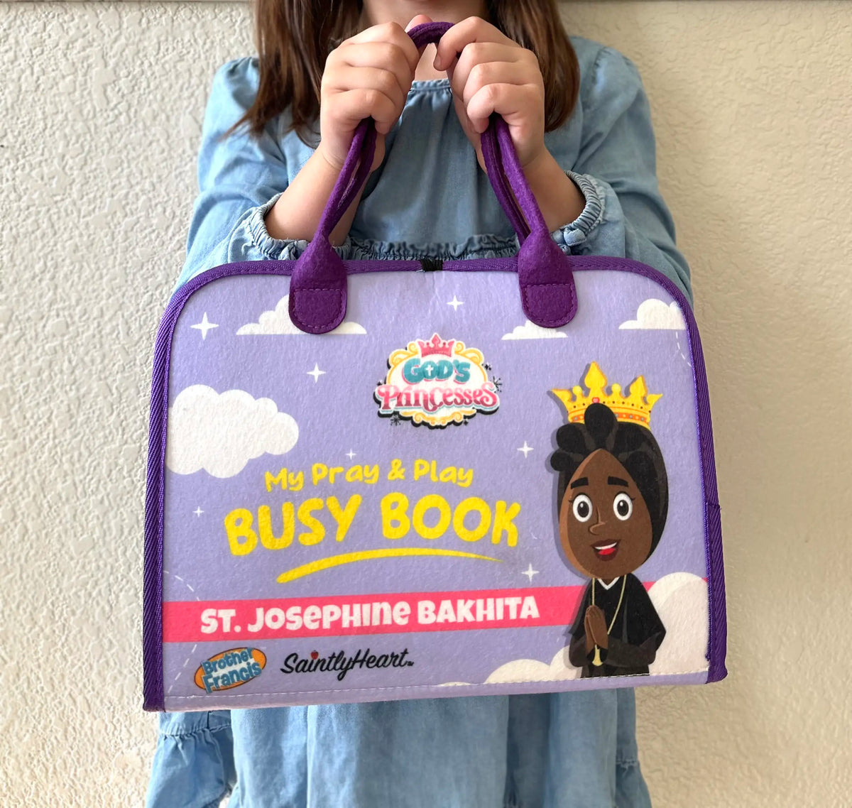girl holding purple felt busy book with saint bakhita on cover